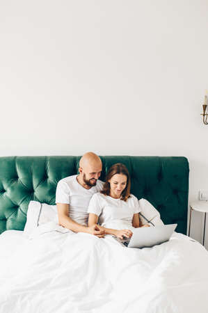 young couple using laptop together in bed