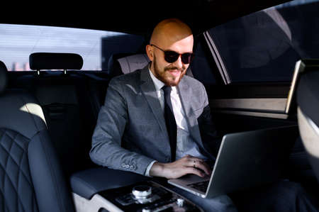 Handsome businessman sitting with laptop on the backseat of the car. travelling by a car and working...