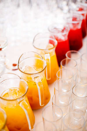 Different types of summer drinks in glasses, cubes of ice and slice of fruits on blue table. Healthy vitamin fruit and berry drinks.の写真素材