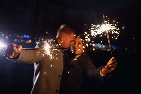 Selective focus of sparklers in hands of young couple enjoying holiday time outdoors