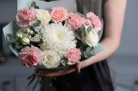 Close-up flowers in hand. Florist workplace. Woman arranging a bouquet with roses, chrysanthemum,...