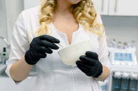  A female doctor-cosmetologist in a white coat holds a bottle of enriched argan oil. Woman with a pipette. Facial care product. Cosmetology room.の写真素材