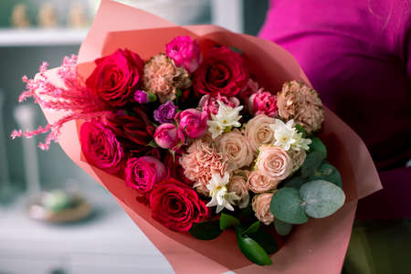 Close-up flowers in hand. Florist workplace. Woman arranging a bouquet with roses, chrysanthemum, carnation and other flowers. A teacher of floristry in master classes or courses.の写真素材