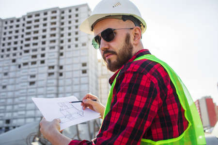Engineering Consulting People on construction site holding blueprint in his hand. Building inspector