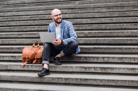 Outdoor office. Modern man in formal suit and sitting on outdoor office stairs. Man using laptopの写真素材