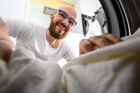 Young man using washing machine at home. Laundry dayの写真素材
