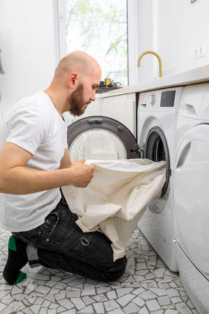 Young man using washing machine at home. Laundry dayの写真素材