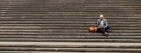 young businessman with laptop sitting on stairs rampの写真素材