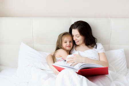 a young mother reads a book in bed to her child