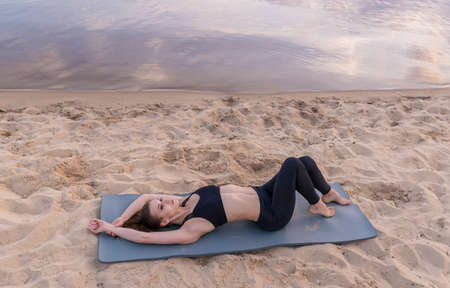 young girl on the seashore on the sand lies on a yoga mat