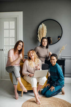 a group of girlfriends watch the series on a laptop. Funny friends of different nationalities at home using laptopの写真素材