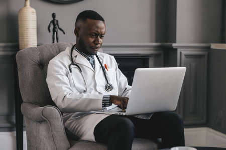 black doctor Using Laptop To Communicate with a patient. Smiling male african american professional young doctor.の写真素材
