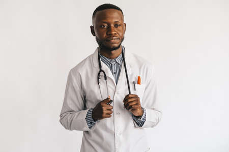 Closeup picture of young African American doctor standing in white uniform against white backgroundの写真素材