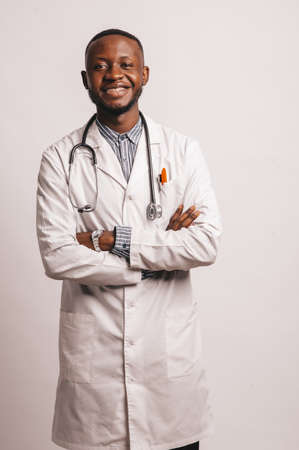 Closeup picture of young African American doctor standing in white uniform against white backgroundの写真素材