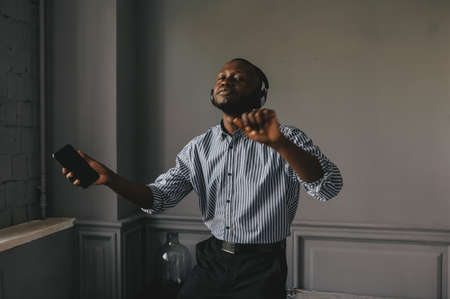 Young african man listening to music with wireless earphones and dancing at homeの写真素材