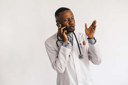 An African-American black young doctor in a white coat is talking on the phone. isolatedの写真素材