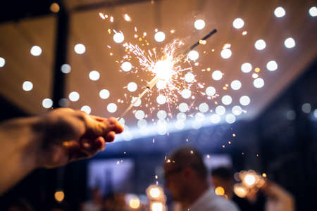 Bengal lights in male hands set fire to each other on Christmas tree lights backgroundの写真素材