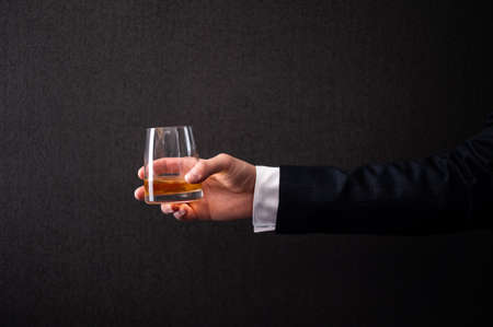a man in a jacket holds a glass of whiskey in his handの写真素材