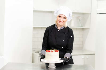 Portrait of friendly smiling female professional confectioner topping a cupcake with cream using a pastry bagの写真素材