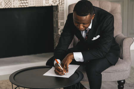 african american businessman in a suit makes notes on a sheet of paper while sitting in his office...