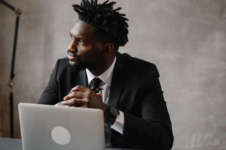 Front view head shot young smiling african american businessman looking at laptop screen, reading pleasant messages in social networks, working on computer sitting at table in office home.の写真素材