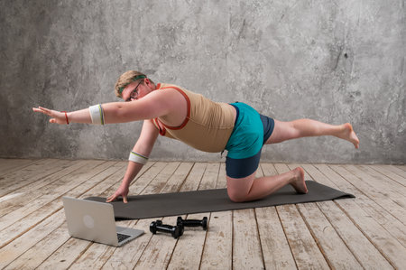 Funny fat man in sportswear doing sports exercises looking into a laptop. home workoutの写真素材