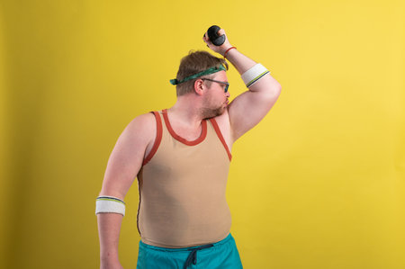 funny fat man doing exercises with dumbbells. Overweight. yellow background