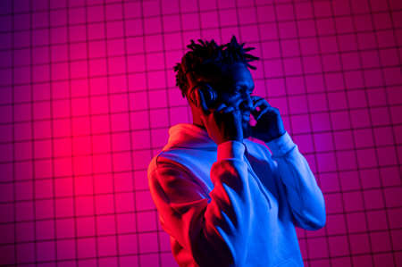 the concept of music. A black man listens to music with headphones on against a background of neon light. Red and blue backgroundの写真素材