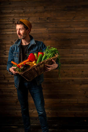 young farmer holds a wicker basket with fresh organic vegetables. small business. Studio shotの写真素材