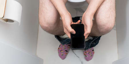 Man using mobile phone in toilet. Internet addiction or social media addictionの写真素材