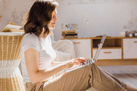 Attractive African-American girl uses laptop and smiles while sitting on the floor