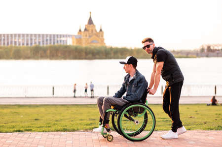 Help for people with physical disabilities. Man drive wheelchair and help his friend. Social services for population.の写真素材