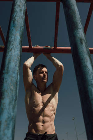 Muscular man during his workout on the street with horizontal bar
