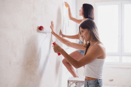 a happy woman makes repairs at home. friends paint the walls in a new apartmentの写真素材