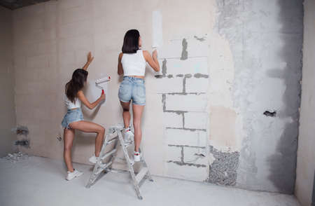 Happy young women doing repair in their new house. Paint the wallsの写真素材