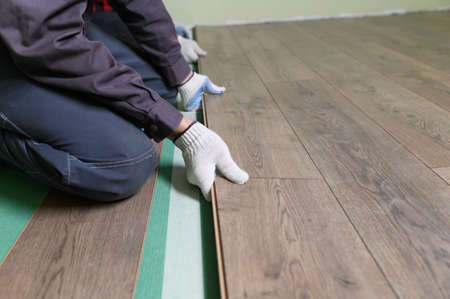 Worker lays the laminate in the apartment. Laminate is lying on the floor in the apartment, the master takes a bar of laminate and puts it on the floor.の写真素材