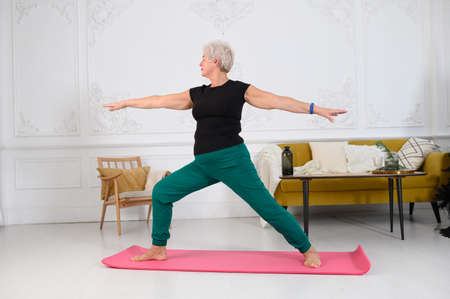 a beautiful looking aged woman does yoga at home in a beautiful white interiorの写真素材