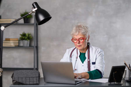 Middle age female doctor using laptop, writing notes with stethoscope on table. Healthcare concept. Medical doctor writing and taking notes.の写真素材