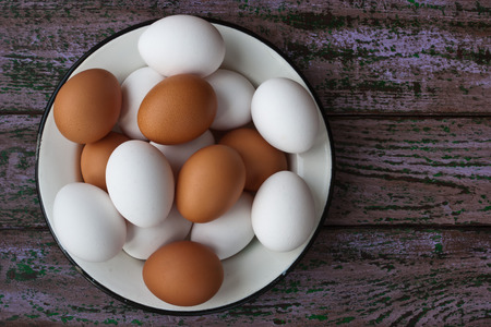 Chicken eggs in a glass and a metall dish on the purple aged boards