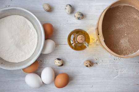 Eggs, flour and a bottle of olive oil on the white wooden table horizontalの写真素材