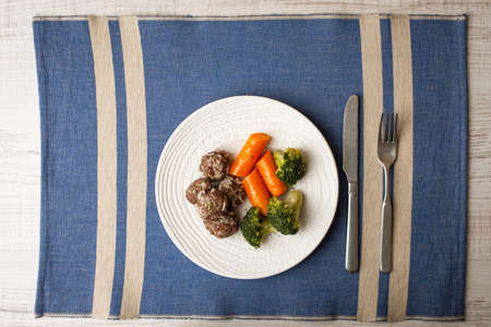 Steamed meatballs and vegetables on the blue napkin with cutlery top viewの写真素材