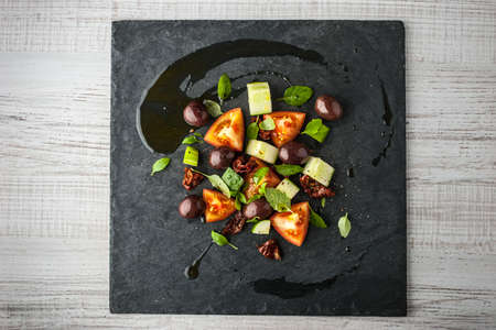Vegetable salad with dried tomatoes and olive on the black stone top viewの写真素材