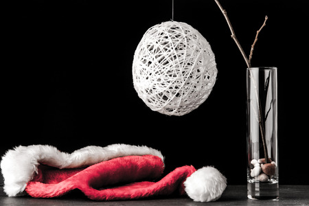 Alder branch in the glass with a white christmas ball and santa claus hat on the black stone table horizontalの写真素材