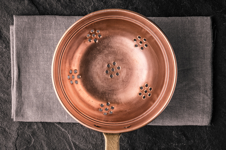 Copper colander on the dark stone table top viewの写真素材