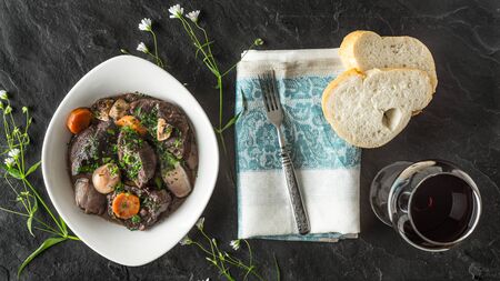 Beef bourguignon in a ceramic plate on a black stone and flower horizontal