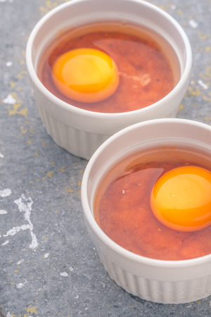 Raw eggs with tomatoes in the ramekins on the stone tableの写真素材
