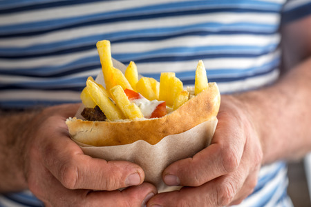 Gyros with french fries in a napkin in the hands of a man on striped backgroundの写真素材