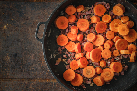 Carrots and bacon in the pan on the metal backgroundの写真素材