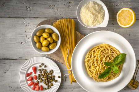 Raw and cooked spaghetti with different appetizer on the white wooden table top view. Concept of Italian cuisineの写真素材