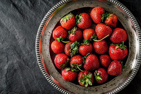 Strawberry in the old metal plate on the black stone table  top viewの写真素材